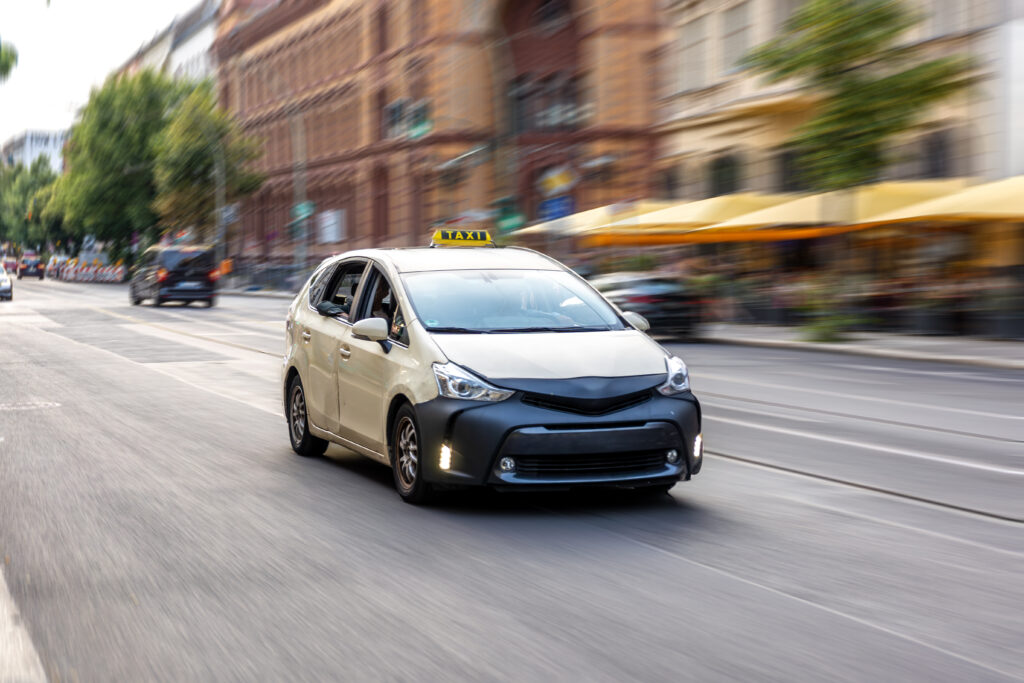 Light-colored taxi moving along a bustling urban street with motion blur effect, conveying fast-paced city dynamics and transport service. Image Courtesy: Freepik